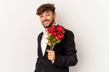 Beyaz arka planda soyutlanmış gül buketi tutan melez genç adam gülümsüyor ve keyifli görünüyor..