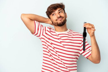 Kol saati tutan genç melez adam mavi arka planda izole edilmiş kafasının arkasına dokunuyor, düşünüyor ve bir seçim yapıyor..