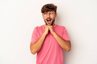 Gri arka planda izole genç melez adam ellerini çenesinin altında tutuyor, mutlu bir şekilde yana bakıyor..