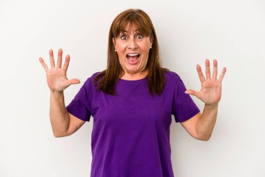 Beyaz arka planda izole edilmiş orta yaşlı beyaz bir kadın hoş bir sürprizle karşılaşıyor, heyecanlı ve el kaldırıyor..