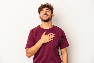 Gri arka planda yaşayan genç melez adam elini göğsünde tutarak kahkahalar atıyor..