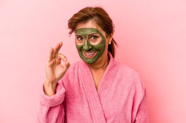 Middle age caucasian woman wearing a facial mask isolated on pink background cheerful and confident showing ok gesture.