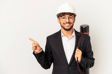 Gri arka planda izole edilmiş bir kask takan genç mimar gülümsüyor ve boş alanda bir şeyler gösteriyor..