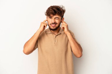 Genç melez adam gri arka planda izole edilmiş kulakları elleriyle kapatıyor..