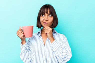 Mavi arka planda pembe kupa tutan genç bir ırk kadını şüpheli ve şüpheci bir ifadeyle yana bakıyor..