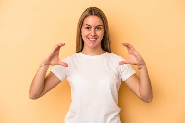 Sarı arka planda izole edilmiş genç beyaz kadın elinde avuç içi bir şeyle kameraya sunuyor..