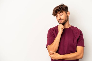 Genç melez adam gri arka planda izole edilmiş şüpheli ve şüpheci bir ifadeyle yana bakıyor..