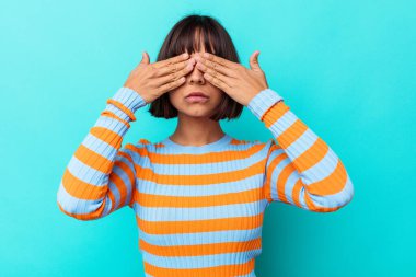 Mavi arka planda soyutlanmış genç melez bir kadın elleriyle gözlerini kapatmaktan korkuyor..