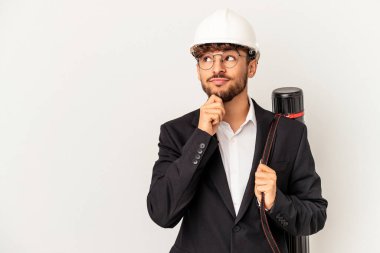 Gri arka planda izole edilmiş kask takan genç mimar şüpheli ve şüpheci bir ifadeyle yana bakıyor..