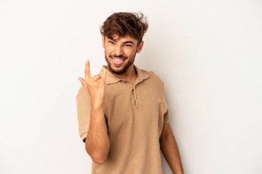 Genç melez adam gri arka planda izole edilmiş, parmaklarıyla kaya hareketi gösteriyor.