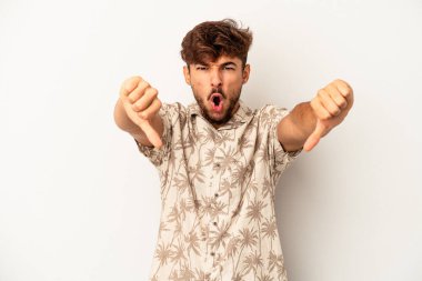 Gri arka planda izole edilmiş genç melez adam baş parmağını aşağı gösteriyor ve hoşlanmadığını ifade ediyor..