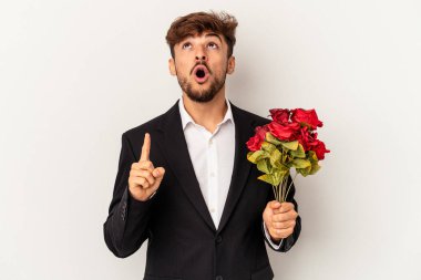 Genç melez adam elinde gül buketi ile beyaz arka planda izole edilmiş ağzı açık bir şekilde üst tarafı işaret ediyor..