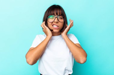 Genç melez kadın mavi arka planda izole edilmiş kulakları parmaklarıyla kaplayan, stresli ve çaresiz gürültülü bir ortam tarafından.