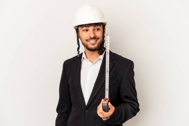 Miğfer takan ve gri arka planda taksimetre tutan genç mimar gülümseyen, neşeli ve keyifli görünüyor..