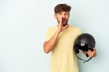 Mavi arka planda izole edilmiş motosiklet kaskı tutan genç melez adam gizli bir sıcak fren haberinin olduğunu söylüyor.