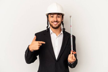 Miğfer takan ve taksimetre tutan genç bir mimar gri arka plandaki izole edilmiş, gömlek fotokopi alanını işaret ediyor, gururlu ve kendinden emin.