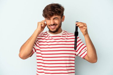 Kol saati tutan genç melez adam mavi arka planda izole edilmiş kulakları elleriyle kapatıyor..