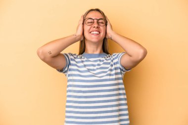 Sarı arka planda izole edilmiş genç beyaz kadın ellerini başının üstünde tutarak neşe içinde gülüyor. Mutluluk kavramı.