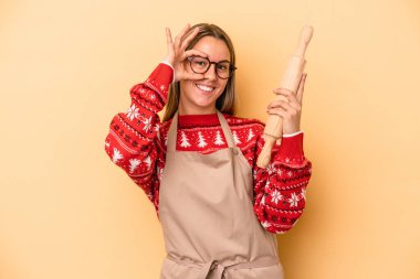 Genç fırıncı kadın Noel için kurabiye yapıyor. Sarı arka planda izole edilmiş. Heyecanlı..