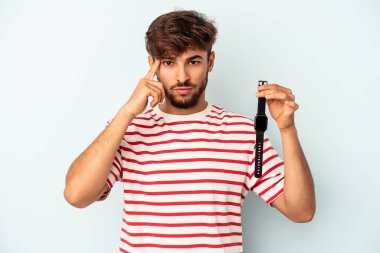 Mavi arka planda izole edilmiş bir kol saati tutan genç melez bir adam şakağı parmağıyla işaret ediyor, düşünüyor ve bir göreve odaklanıyor..