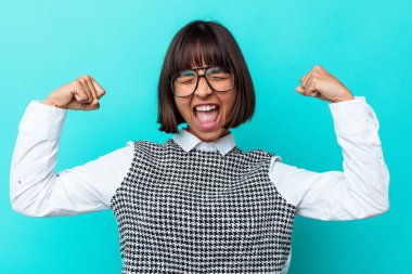 Genç melez kadın mavi arka planda izole edilmiş zaferden sonra yumruğunu kaldırıyor, kazanan konsept..