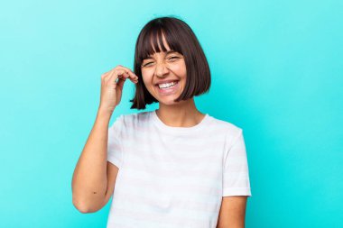 Mavi arka planda izole edilmiş genç bir ırk kadını bir şeye gülüyor, elleriyle ağzını kapatıyor..