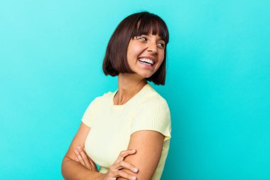 Mavi arka planda soyutlanmış genç melez bir kadın kollarını kavuşturarak gülümsüyor..