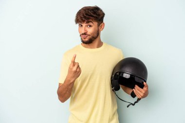 Mavi arka planda izole edilmiş motosiklet kaskı tutan genç melez seni parmağıyla işaret ediyor sanki davet ediyormuş gibi..