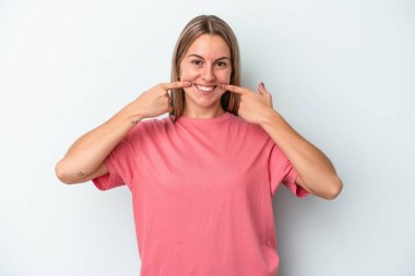 Mavi arka planda izole edilmiş genç beyaz kadın gülümsüyor, parmaklarını ağıza doğrultuyor..