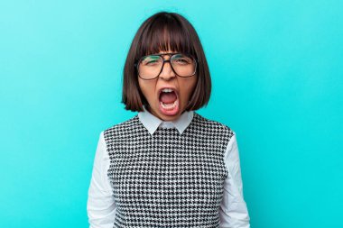 Mavi arka planda izole edilmiş genç bir ırk kadını çok kızgın, öfkeli ve sinirli bir şekilde bağırıyor..