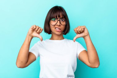 Mavi arka planda izole edilmiş genç melez kadın baş parmağını aşağı gösteriyor, hayal kırıklığı konsepti..