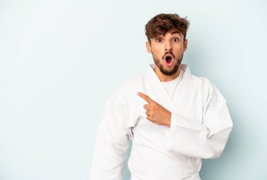 Genç melez karate yapıyor. Mavi arka planda izole edilmiş. Yan tarafı işaret ediyor.
