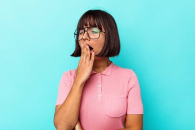 Mavi arka planda soyutlanmış genç melez bir kadın esniyor. Ağzıyla ağzını kapatan yorgun bir hareket sergiliyor..