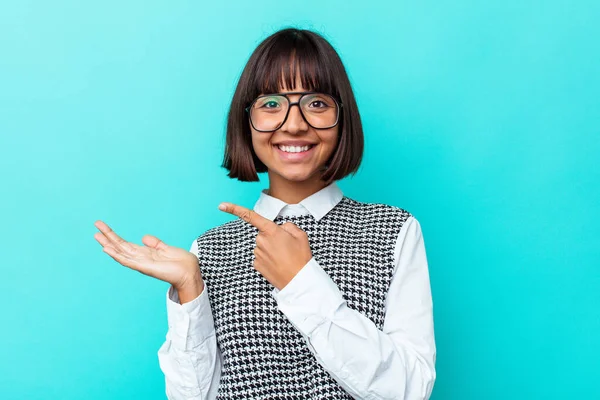 Mavi arka planda izole edilmiş genç melez bir kadın. Elinde bir kopya tutarken heyecanlanıyor..