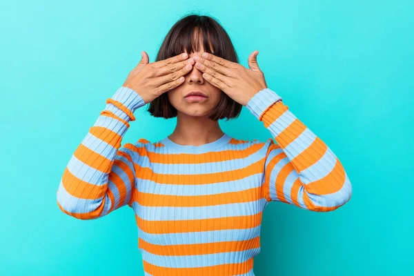 Mavi arka planda soyutlanmış genç melez bir kadın elleriyle gözlerini kapatmaktan korkuyor..