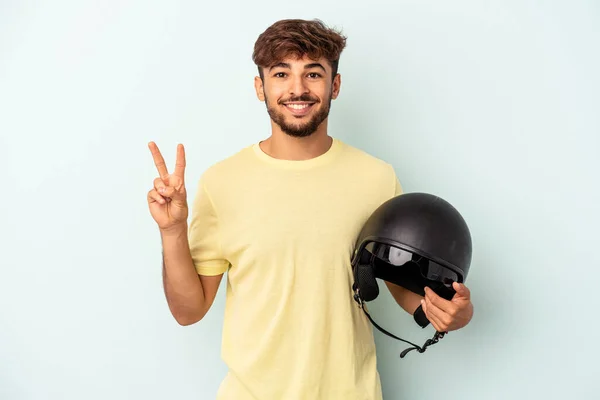 年轻的混合赛男子手持摩托车头盔 蓝色背景显示他的手指是二号 — 图库照片