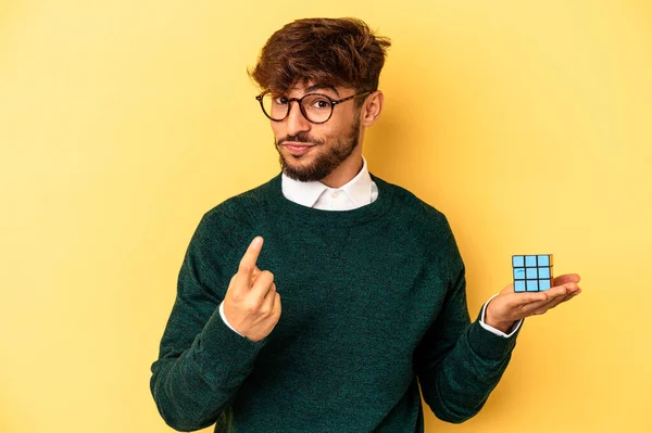 Mladý Míšenec Drží Rubiks Kostku Izolovanou Žlutém Pozadí Ukazuje Prstem — Stock fotografie