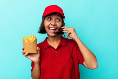 Genç melez ırk fast food restoranı çalışanı mavi arka planda izole edilmiş patates kızartması tutuyor ve parmaklarıyla bir cep telefonu hareketi gösteriyor..