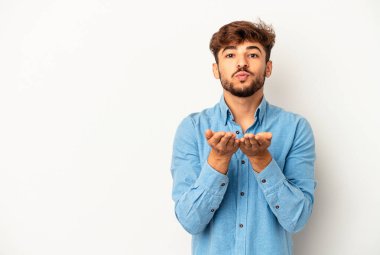 Genç melez adam gri arka planda izole edilmiş dudaklar kıvrılıyor ve hava öpücüğü göndermek için avuç içi tutuyor..
