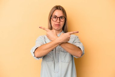 Sarı arka plan noktalarında izole edilmiş genç beyaz kadın iki seçenek arasında seçim yapmaya çalışıyor..