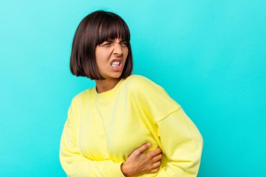 Genç melez kadın mavi arka planda izole edilmiş sırt ağrısı çekiyor..