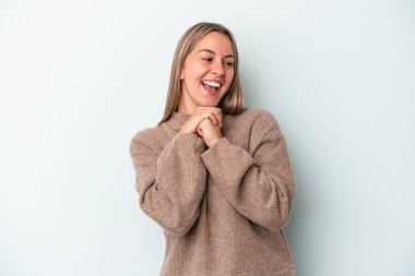 Mavi arka planda izole edilmiş genç beyaz kadın ellerini çenesinin altında tutuyor, mutlu bir şekilde yana bakıyor..