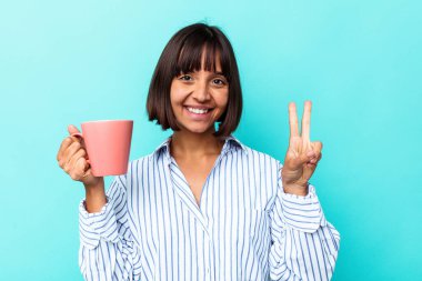 Mavi arka planda pembe kupa tutan genç melez kadın iki numarayı parmaklarıyla gösteriyor..