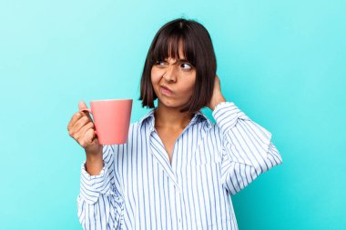 Mavi arka planda pembe kupa tutan genç melez kadın kafasının arkasına dokunuyor, düşünüyor ve bir seçim yapıyor..