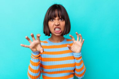 Mavi arka planda izole edilmiş genç melez kadın pençelerini kedi taklidi yaparken gösteriyor, agresif bir hareket..