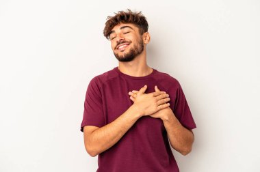 Gri arka planda izole edilmiş genç melez adam, avuçlarını göğsüne bastıran dostane bir ifadeye sahiptir. Aşk konsepti.