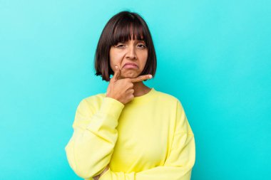 Genç melez kadın, mavi arka planda izole edilmiş. Bir strateji planlıyor, bir iş yolu düşünüyor..