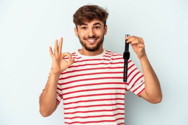 Kol saati tutan genç melez adam mavi arka planda izole edilmiş neşeli ve kendinden emin..