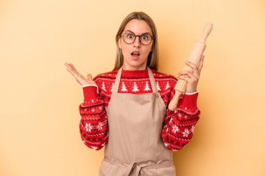 Genç fırıncı kadın Noel için kurabiye yapıyor. Sarı arka planda izole edilmiş. Şaşırmış ve şok olmuş..