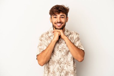 Gri arka planda izole genç melez adam ellerini çenesinin altında tutuyor, mutlu bir şekilde yana bakıyor..